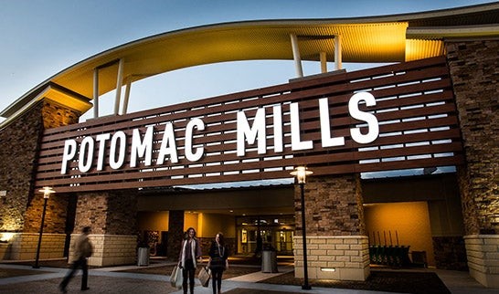 otomac Mills Mall illuminated entrance sign with visitors walking during the evening.