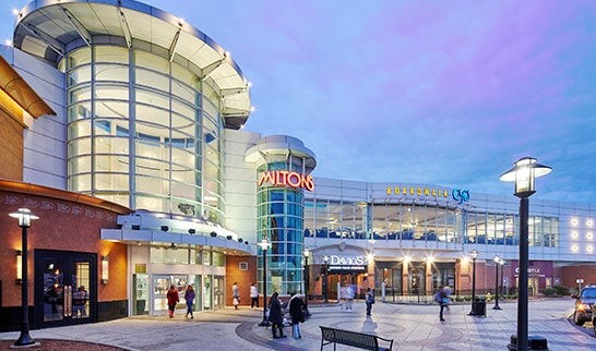 Exterior view of South Shore Plaza Mall during the evening with vibrant lighting and shoppers walking near the entrance.